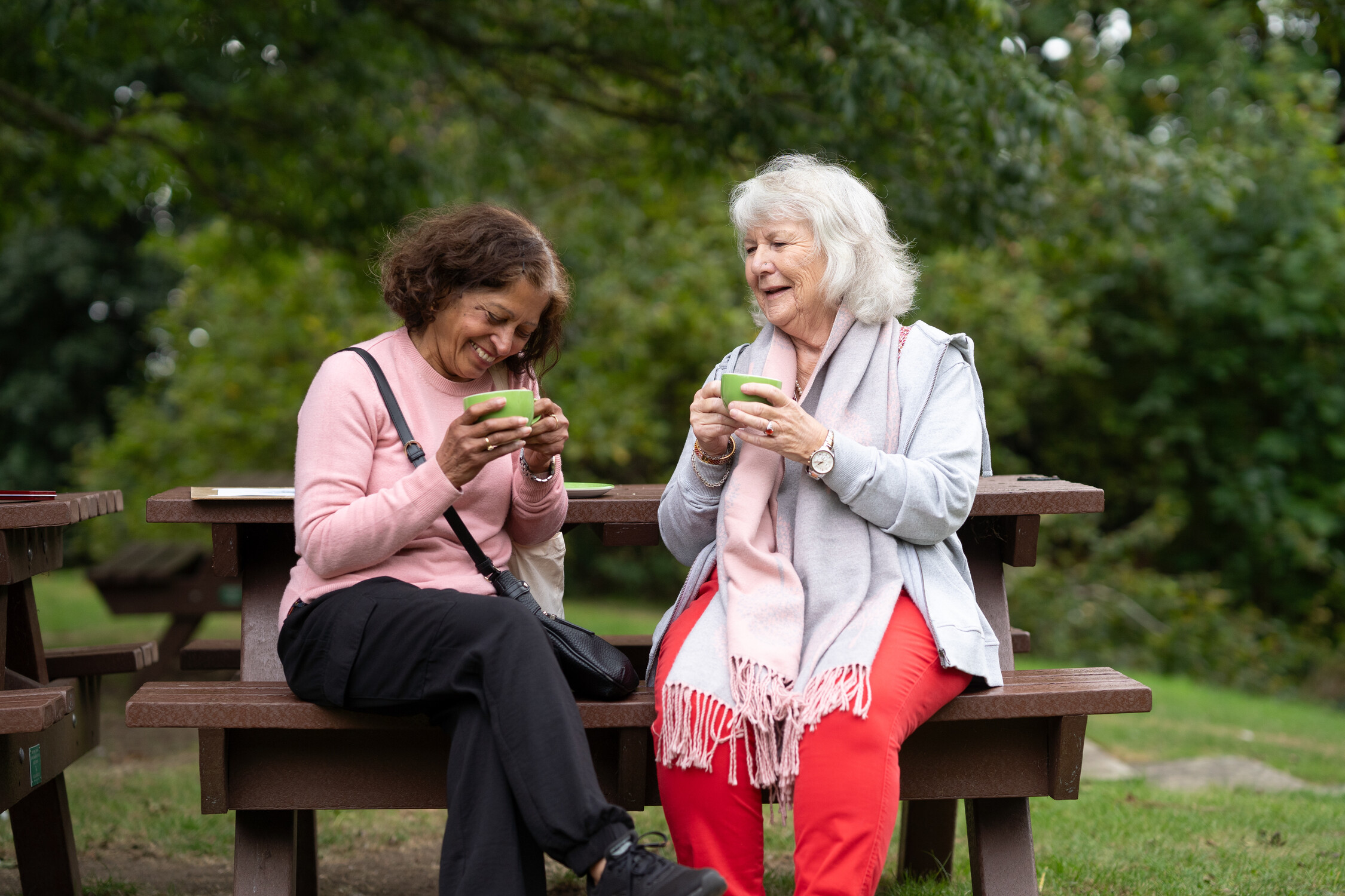 Two women sit on a park bench and enjoy a cup of tea.